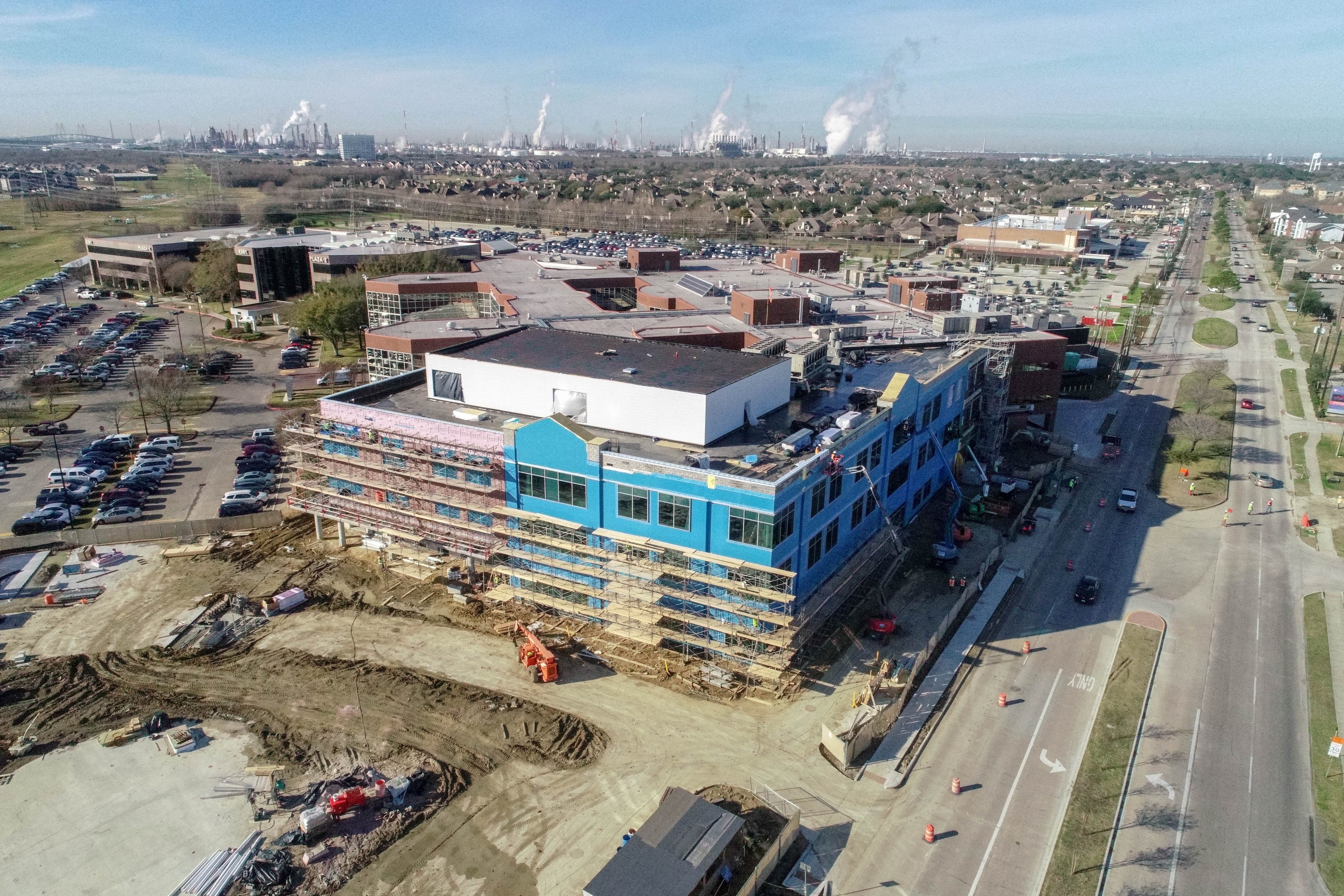 Aerial photograph of a building under construction. Industrial refineries area in the background.